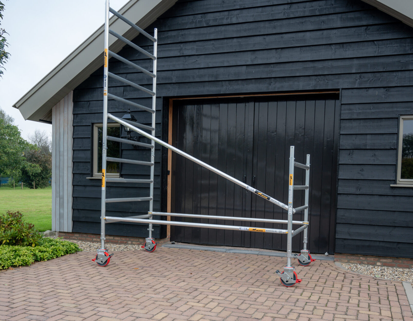Een Wixor rolsteiger met schoren wordt opgebouwd met op de achtergrond een schuur